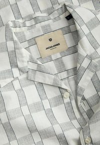 Camisa de manga corta con patrón a cuadros en blanco y azul marino. Fabricada en un material ligero con una textura suave. Cuenta con una etiqueta con el logotipo de la marca.