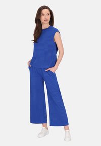 Blå mönstrad tvådelad dräkt bestående av en ärmlös topp och vida byxor, tillverkad av texturerat tyg med sidofickor.