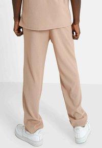 Beige geribde broeken met een relaxte pasvorm, uitgerust met een elastische tailleband en subtiele textuur, gecombineerd met witte sneakers.