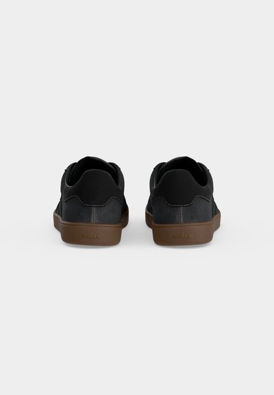 Paire de baskets basses noires avec semelles marron, vues de dos, montrant les détails de couture et le logo "HOGAN" sur chaque semelle.