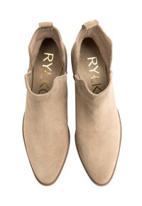 Beżowe zamszowe botki za kostkę o gładkiej fakturze, w kształcie szpiczastym, z wycięciami po bokach. Złote logo widoczne na wkładce. Płaska gumowa podeszwa.