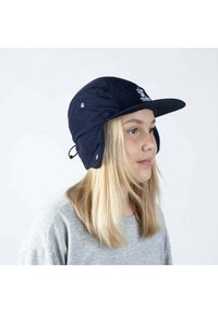 Laivaston sininen talvilakki, jossa on etu lippa ja korvaläpät, valmistettu pehmeästä kankaasta. Sisältää logon ja nepparit sivuilla.