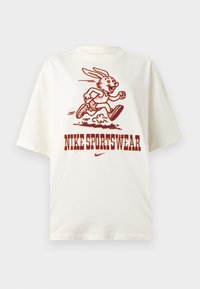 Λευκή μπλούζα με φανταστικό λαγουδάκι που τρέχει και το κείμενο "NIKE SPORTSWEAR" με έντονα κόκκινα γράμματα κάτω από την εικόνα.