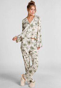 Loungewear set met bloemmotief bestaat uit een lichtgewicht, crèmekleurige top met een losse pasvorm en lange mouwen, gecombineerd met bijpassende broek met patroon en zachte slippers.