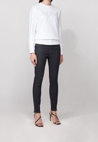 Sweatshirt blanc avec logo "BOSS" en relief, associé à un jean skinny noir et des talons hauts noirs à brides. Design simple et décontracté, coupe moderne.