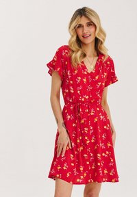 Czerwona sukienka w kwiaty z krótkimi falbaniastymi rękawami, dekoltem w serek, z detalami na guziki i paskiem w talii, ozdobiona żółtymi i różowymi wzorami kwiatowymi.