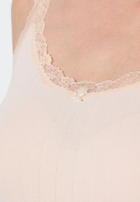 Camisole rosa chiaro con scollatura in pizzo, sottili strisce verticali e un piccolo fiocco al centro. Texture morbida.