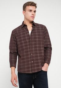 Brun rutete skjorte med lange ermer, med hvite rutenettlinjer og en frontlomme, paret med mørkeblå jeans.