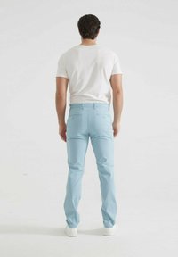 Chinos bleu clair en coton, avec une coupe slim, des poches arrière et une texture lisse. Associés à un t-shirt blanc et des baskets.
