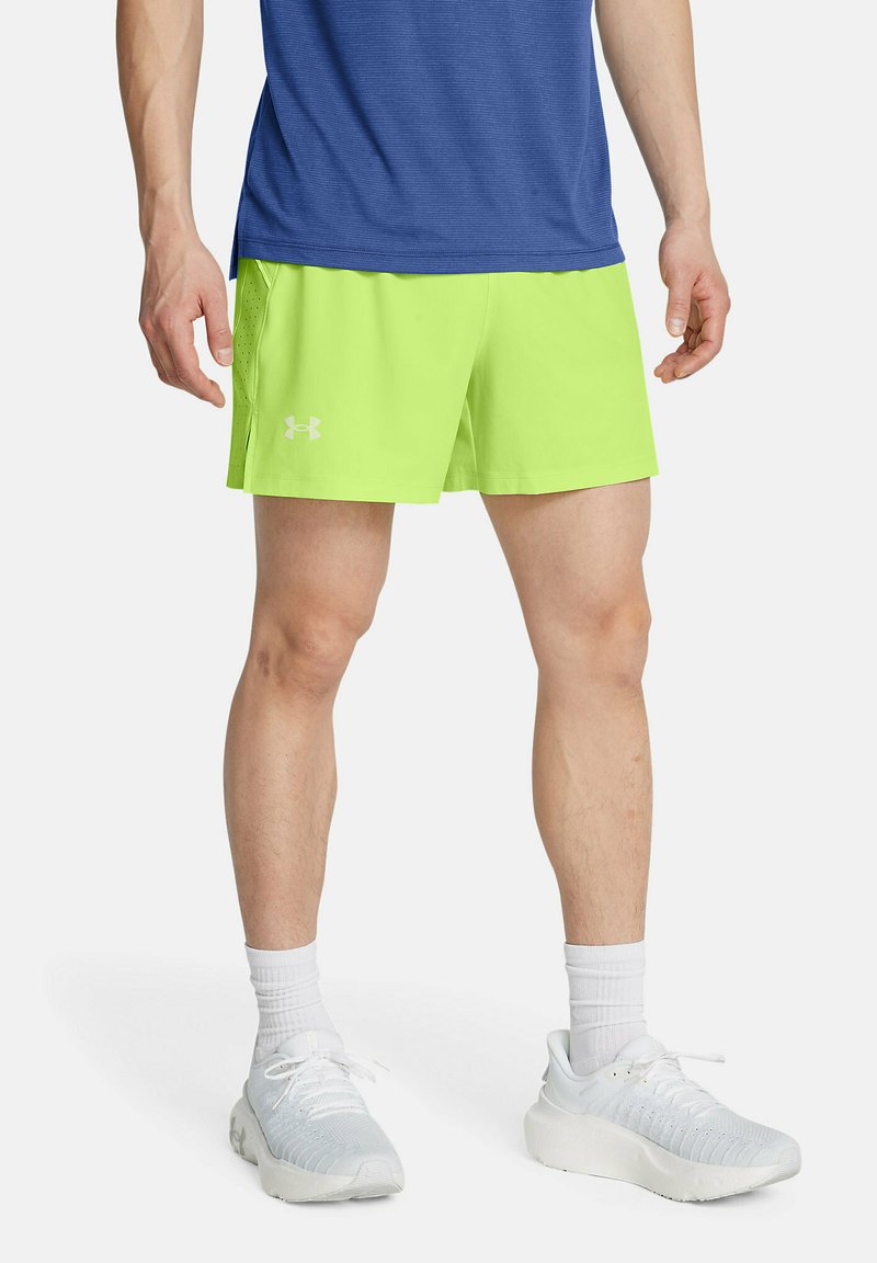 Erksed neoonrohelised lühikesed püksid elastse vöökohtaga, vasakul jalal väikese valge logoga, koos valgete spordijalatsite ja sokkidega.
