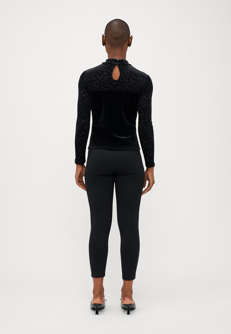 Top nero a maniche lunghe con texture in velluto e accenti di stampa leopardata. Dettaglio a chiave sul retro. Abbina a leggings neri e tacchi a punta.
