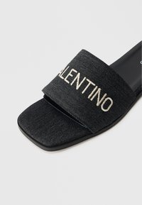 Schwarze Denim-Slide-Sandale mit einem breiten Riemen, auf dem "VALENTINO" in Beige gestickt ist. Quadratische Spitze und glatte schwarze Sohle.