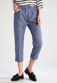 Světle modré, zkrácené kalhoty vyrobené z chambray tkaniny. Mají zapínání na knoflík a ohrnuté manžety, v kombinaci s lesklými černými mokasíny.