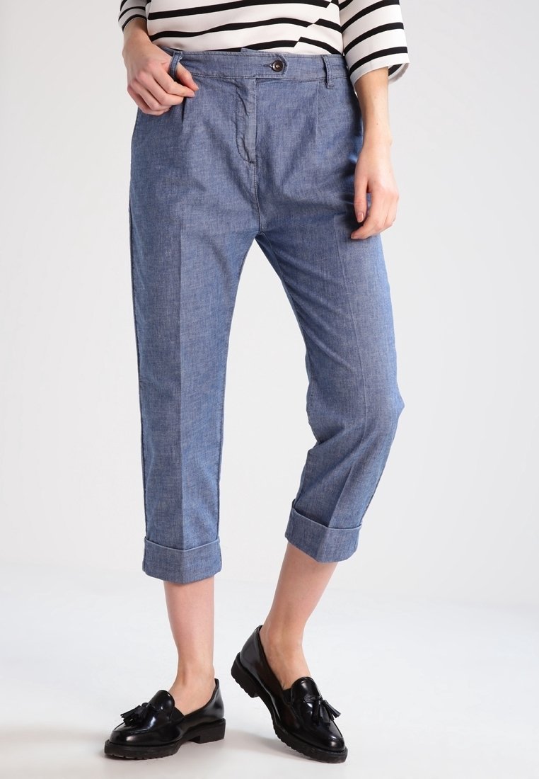 Světle modré, zkrácené kalhoty vyrobené z chambray tkaniny. Mají zapínání na knoflík a ohrnuté manžety, v kombinaci s lesklými černými mokasíny.