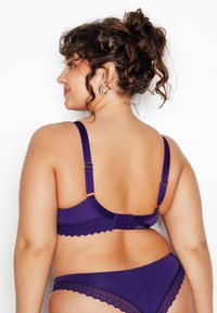 Ensemble de lingerie violet avec bordure en dentelle, bretelles ajustables et fermeture à agrafes dans le dos. Texture lisse qui complète le design.
