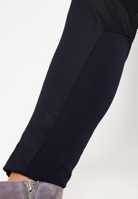 Námořnické kalhoty po kotníky s texturovaným bočním panelem; štíhlý střih s hladkým povrchem. Šedé semišové kotníkové boty se zipovým detailem.