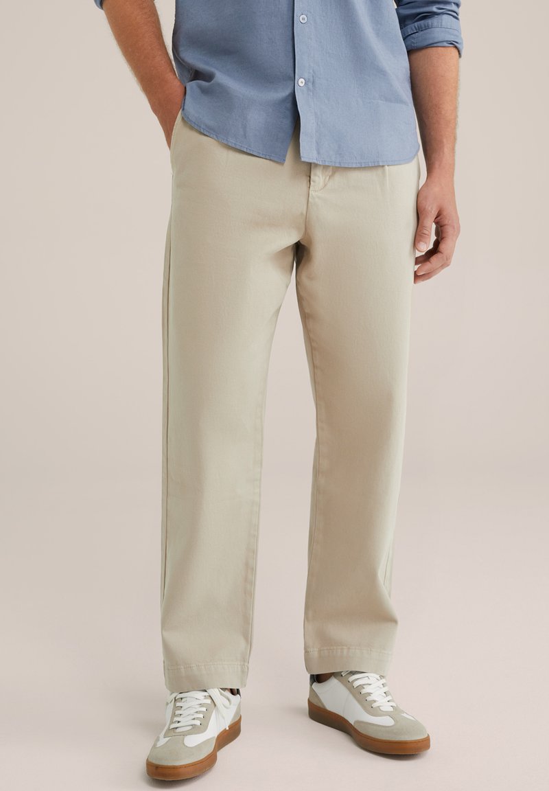 Chinos bej cu o croială dreaptă, realizate dintr-un material de bumbac fin. Asortate cu adidași albi și gri pentru un look casual.