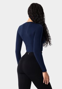 Námornícky dlhý rukáv crop top vyrobený z elastického materiálu v kombinácii s čiernymi legínami s vysokým pásom, ktoré majú jemné textúrované detaily a logo.