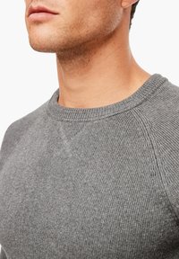 Gros plan sur le bas du visage et le cou d'un homme portant un pull en tricot gris texturé avec un col côtelé et des détails de couture.