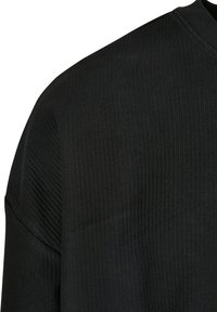 Sort ribbet stofdetalje med en diskret tekstur og en bred udskæring. Beklædningen har korte, afslappede ærmer og en glat overflade.