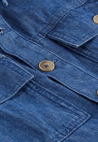 Giacca di jeans blu scuro con dettagli a bottoni, due tasche sul petto con pattina e cuciture a contrasto su un tessuto strutturato.