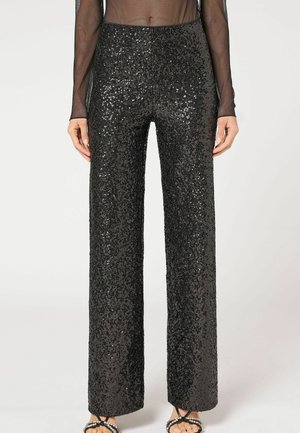 Black high-waist straight-leg pants covered in sequins, worn with sheer long-sleeve top and open-toe sandals with pearl details.