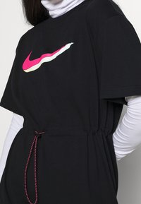 Czarna koszulka z bawełnianej mieszanki o luźnym kroju, z różowo-białym logotypem Nike. Zawiera regulowany sznurek w talii.