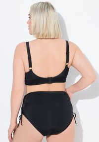 Conjunto de bikini negro que presenta un diseño de espalda baja, tirantes ajustables y parte inferior de cintura alta con lazos laterales. Textura de tela suave y elástica.