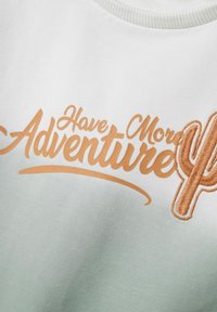 Sweatshirt blanc avec "Have More Adventure" en texte cursif orange, présentant un design de cactus. Texture lisse, col côtelé.