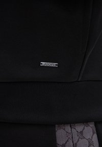 Zwarte sweatshirtstof met geribde zoom en boorden. Bevat een zilveren logotag. Inclusief een patroonsectie met een zachte, gestructureerde afwerking.