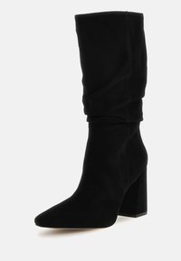 Zwarte kniehoge laars van suède met een spitse neus en blokhak. Heeft een zachte stof en een geplooid ontwerp langs het schacht.