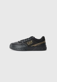 Sapatilhas de couro pretas com detalhes em dourado, acabamentos texturizados e uma sola de borracha grossa. Apresenta atacadores e logotipo na lateral.