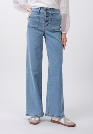 Light blue, high-waisted denim pants with wide legs, five pockets, and a button fly. Soft texture and casual design. Worn with gray sneakers.