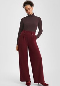 Burgundowe spodnie o szerokich nogawkach z dwoma guzikami na wysokim stanie, połączone z ciemnobrązowym golfem. Gładka tkanina, luźny krój.