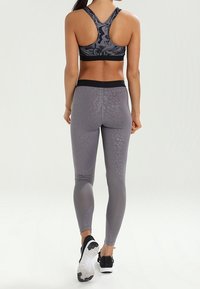 Reggiseno sportivo grigio e leggings abbinati con un motivo testurizzato. Il reggiseno presenta un design con schienale a corsetto, mentre i leggings hanno una vita alta e pannelli a contrasto.
