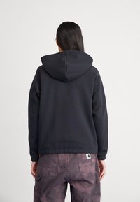 Black hooded sweatshirt made of soft fabric, featuring a relaxed fit and ribbed cuffs. The back displays a logo label above the waistband.