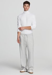 Biała bluzka z golfem zestawiona z luźnymi, jasnoszarymi spodniami dresowymi. Miękka tkanina, luźny krój i elastyczny pasek z troczkiem. Subtelna tekstura na całej powierzchni.