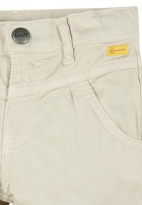 Pantaloni corti in cotone beige con bottone metallico inciso "Steiff", etichetta gialla e cuciture a contrasto. Dettaglio delle tasche frontali incluso.