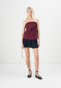 Bordeaux strapless top met elastische rand en strikdetail, gecombineerd met een gelaagde marineblauwe rok, zwarte veterballerina's en een witte tas.