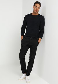 Pulover negru cu nervuri, cu mâneci lungi, asortat cu pantaloni negri subțiri și adidași albi. Puloverul are un model texturat.