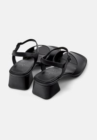 Black heeled sandals with a square toe design, featuring ankle straps and a chunky, low block heel. Made from smooth synthetic material.