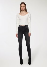 Maglione bianco corto con scollo a V e maniche lunghe, abbinato a jeans skinny grigi scuri a vita alta e stivaletti neri.