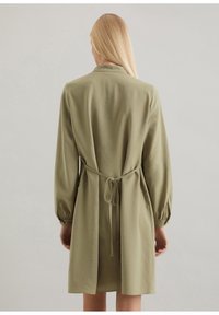 Abito verde oliva, al ginocchio, con maniche lunghe a sbuffo, una cintura in vita e colletto. Tessuto morbido e leggero con una vestibilità rilassata.