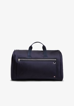 Granatowa torba podróżna z dwoma uchwytami, przednią kieszenią na suwak i małym prostokątnym logo w prawym dolnym rogu.