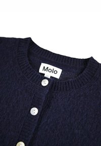 Námořnický pletený kardigan s kulatým výstřihem, pěti knoflíky v řadě a viditelným štítkem značky "Molo" na límci. Texturovaná tkanina.