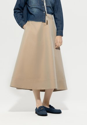 Beige cotton A-line skirt falls to mid-calf; paired with a blue denim shirt and blue loafers with a subtle design detail.
