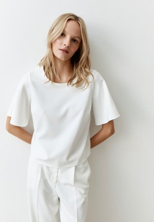 Weißes, kurzärmliges Blusenshirt mit runden Ausschnitt. Glattes Material mit lockerer Passform, getragen mit passenden hellen Hosen. Schlichte Gestaltung.