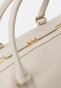 Beige leather handbag with textured surface, gold zippers, and hardware. Features double handles and a structured design.