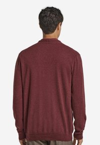 Bordeauxroter Pullover mit klassischem Design, gerippten Bündchen und Saum, aus einem weichen Strickmaterial, mit subtiler Textur und figurbetontem Schnitt.
