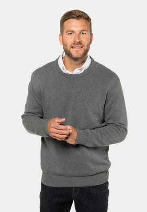 Grå strikket sweater med rund halsudskæring og ribbede manchetter. Båret sammen med mørke jeans, hænderne vist sammen på en neutral baggrund.